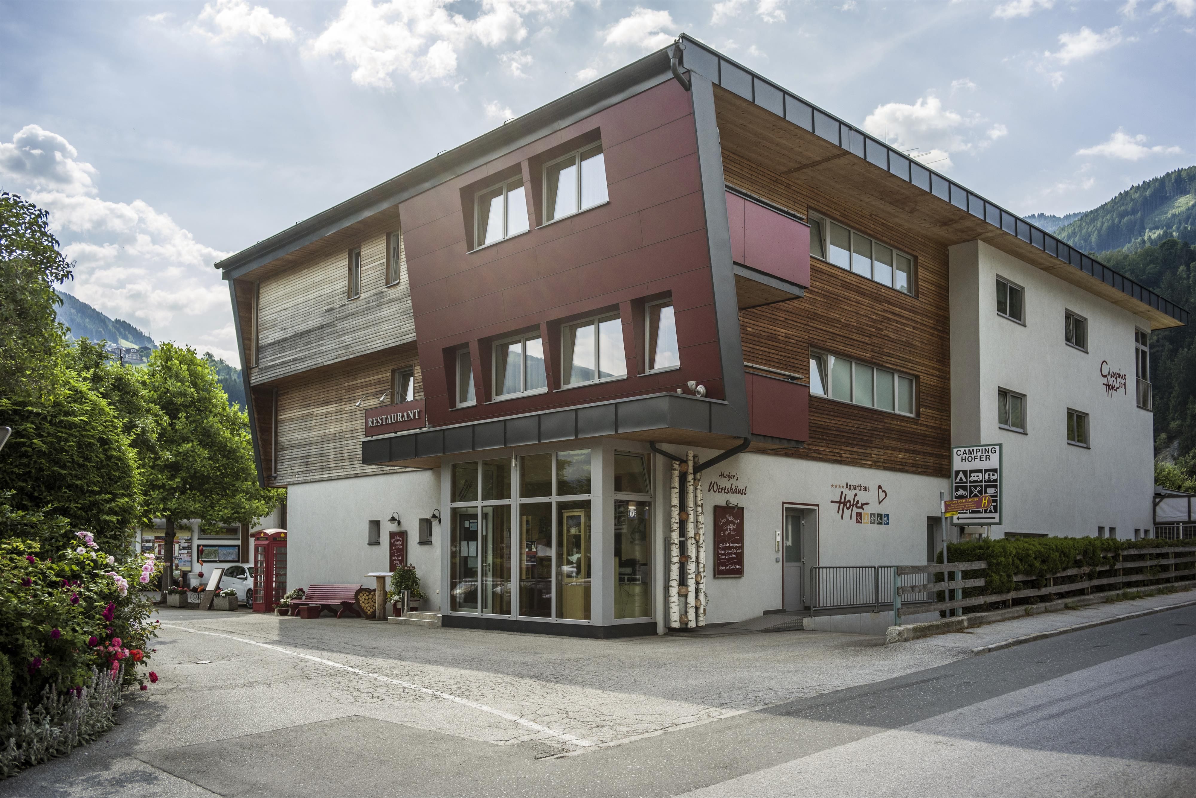A modern building with wooden elements and large windows. It is located in a nature-friendly environment with trees and mountains in the background.