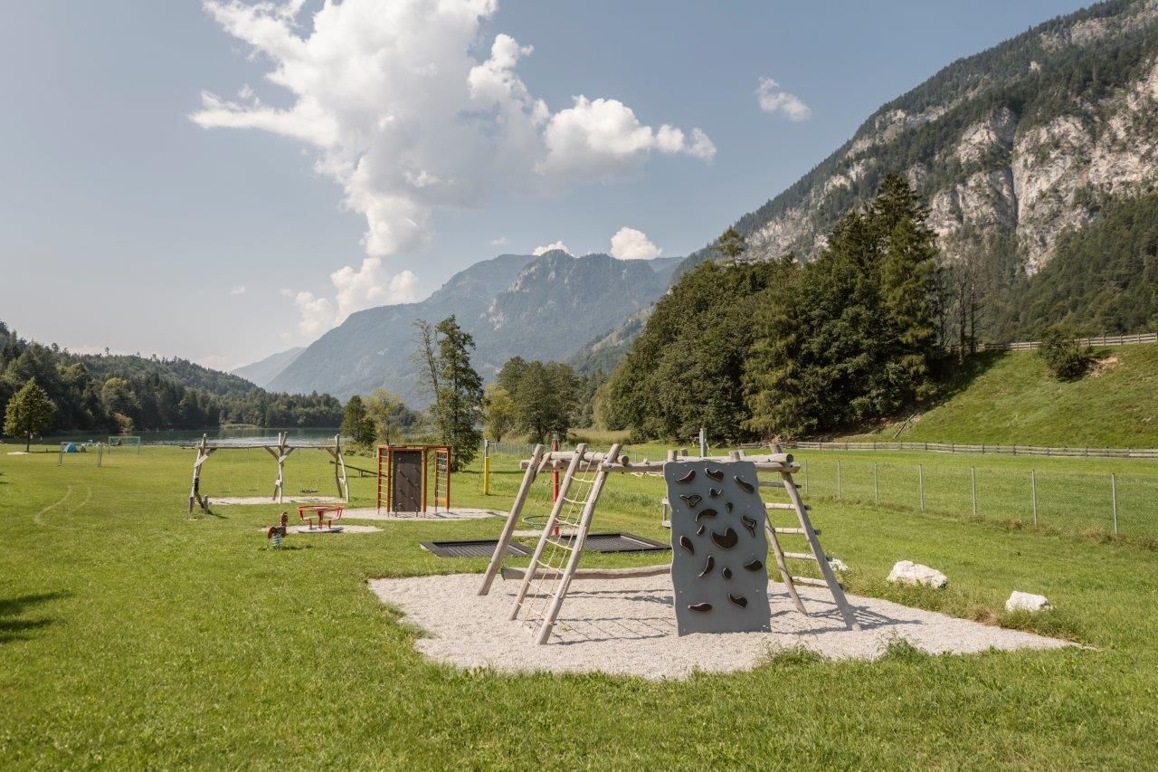 A play area with climbing equipment on a green meadow. In the background, mountains and a blue sky can be seen.