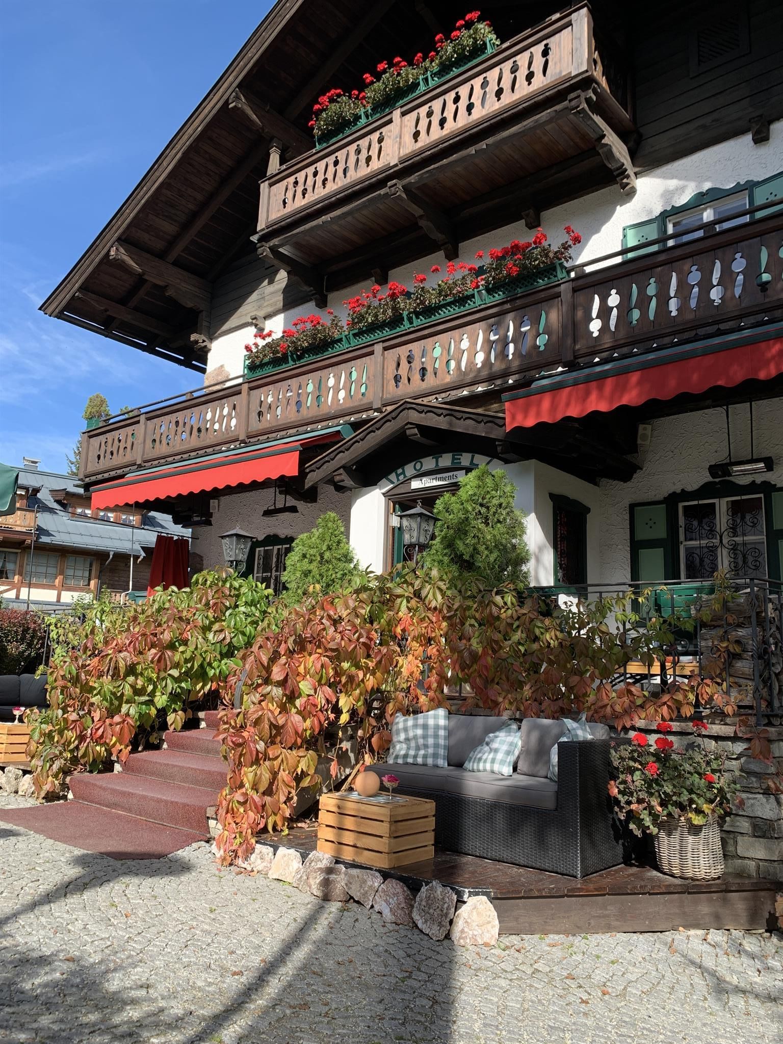 A traditional house with beautiful balconies and blooming plants. In the foreground, there is a cozy seating area with plants.