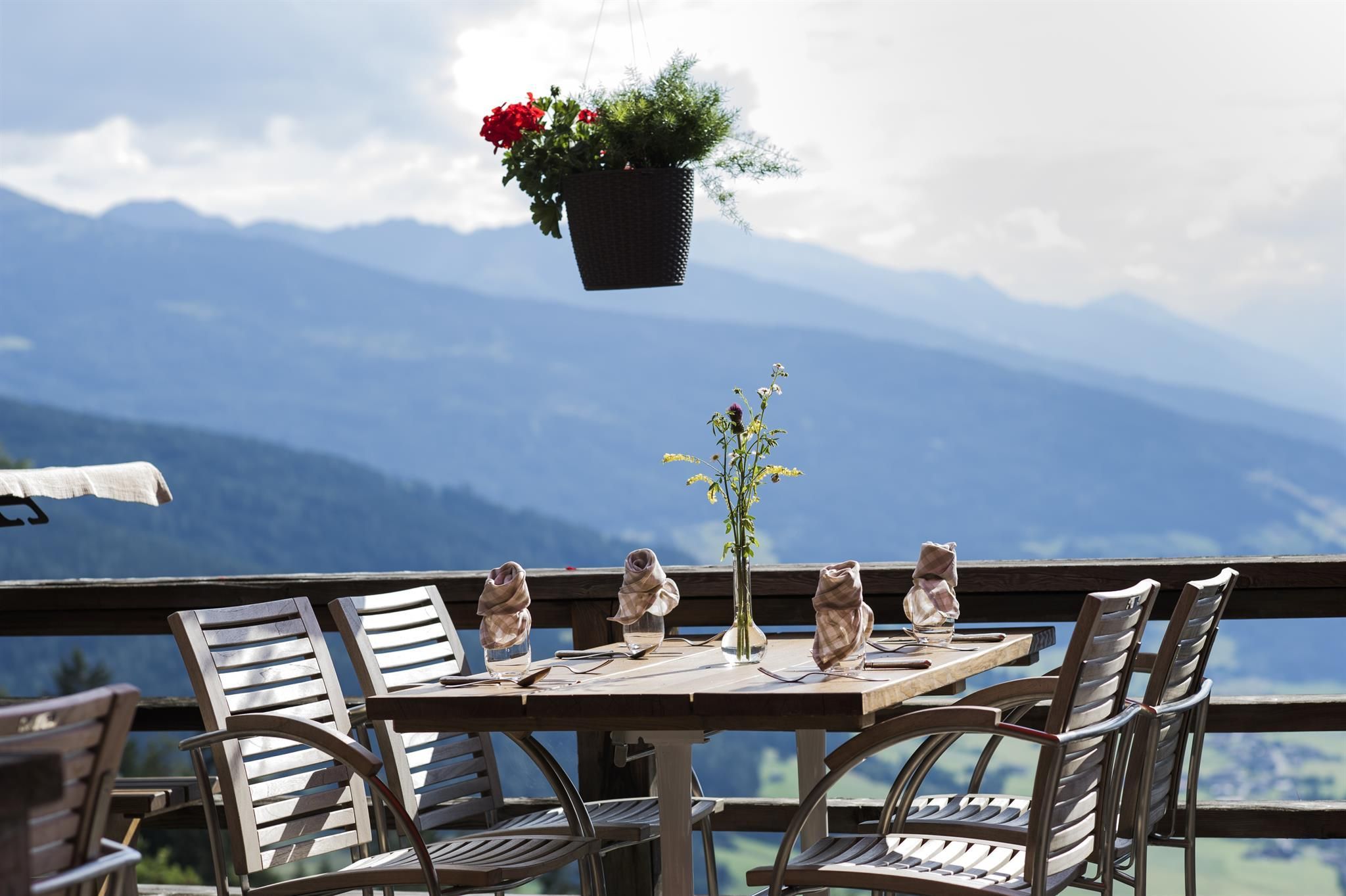 A beautiful table with chairs on a terrace, surrounded by mountains. Flowers and decorated napkins are on the table.