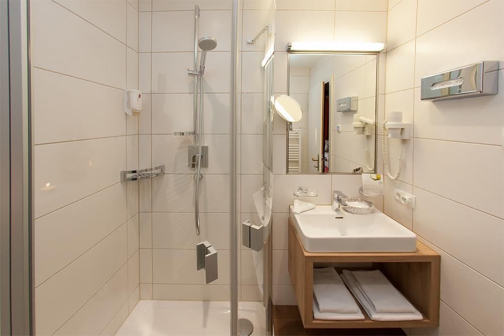 A modern bathroom with a shower and a sink. The walls are light-colored tiled, and the space looks clean and fresh.