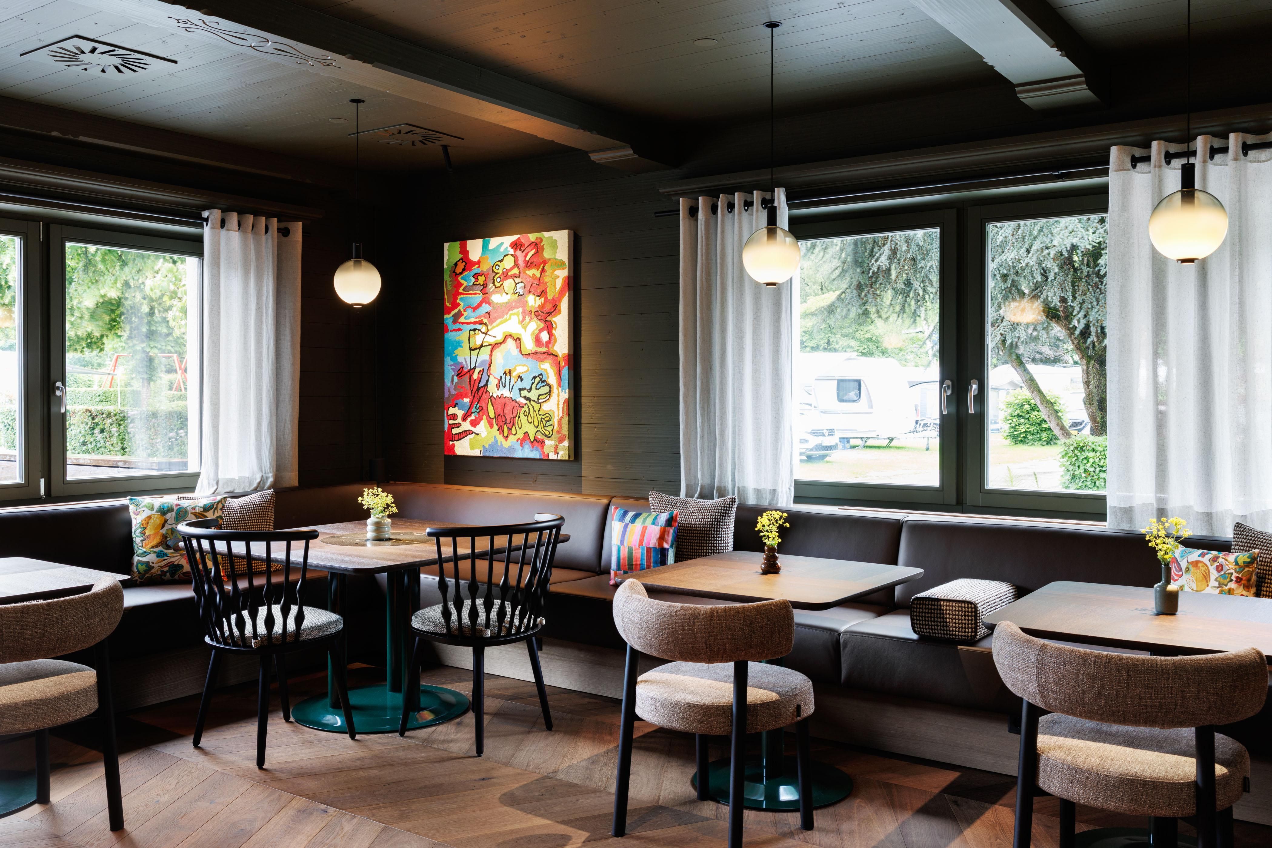 A modern café with cozy seating and colorful decorations. Large windows are hung on the walls, letting in plenty of daylight.