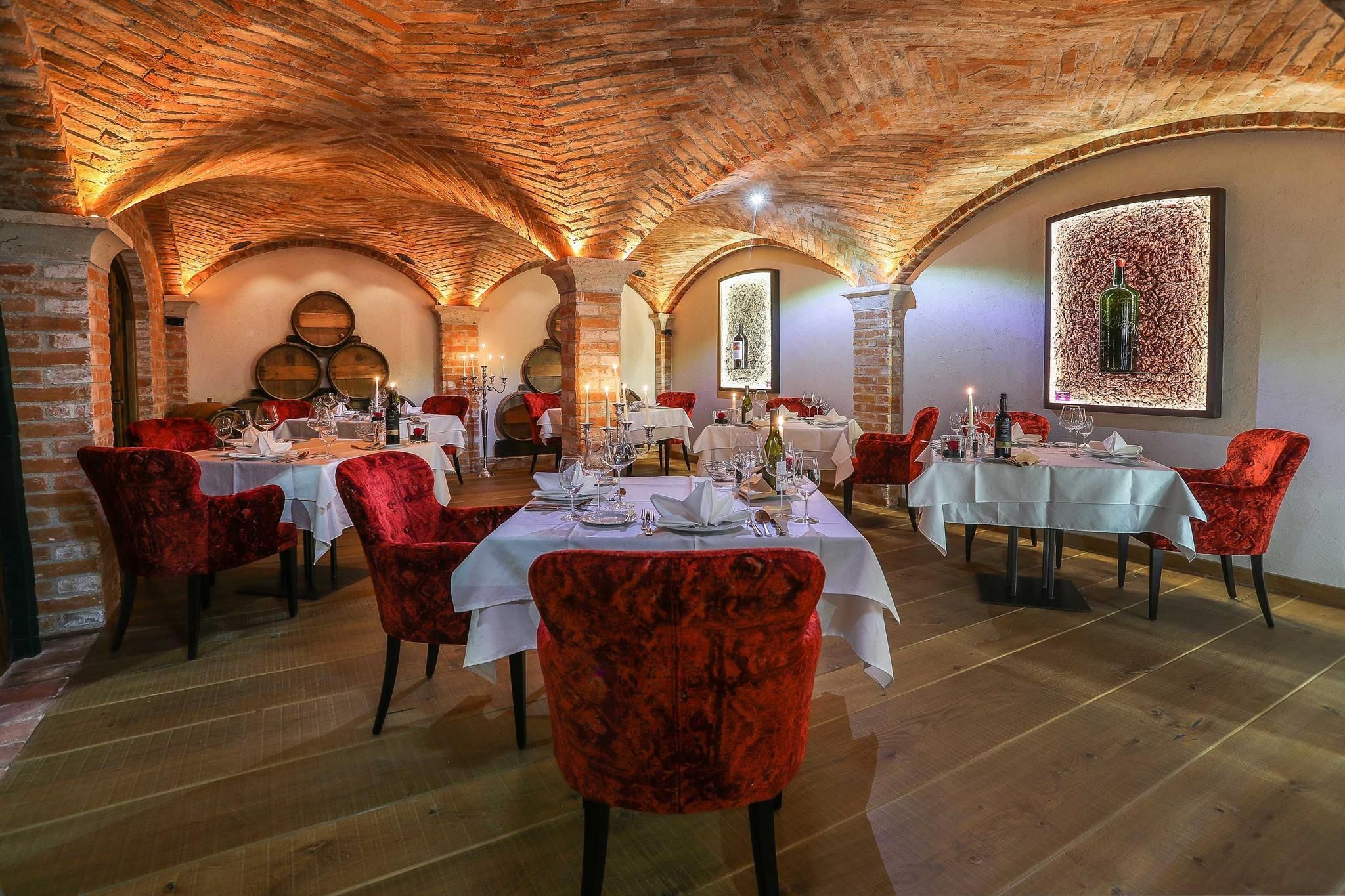 A stylish restaurant with red chairs and elegantly set tables. The atmosphere is warm and inviting with historical stone architecture.